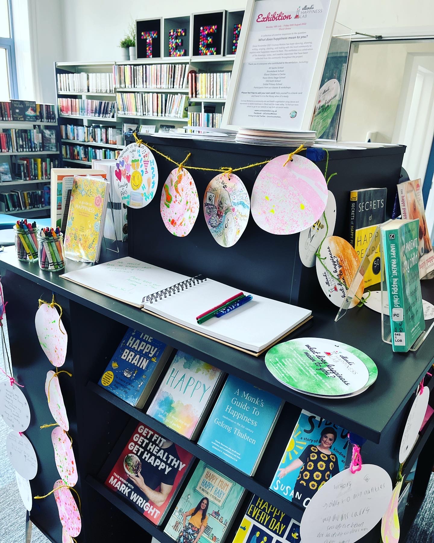 Colourful circular cards surround the exhibition sign and books on happiness